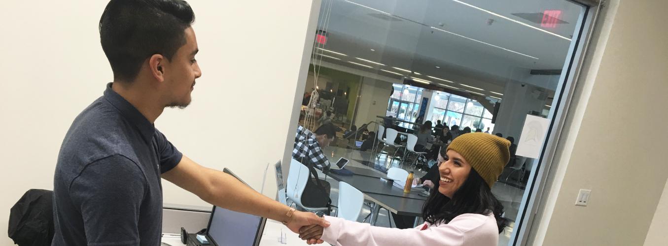 Student shaking hands with person at front desk