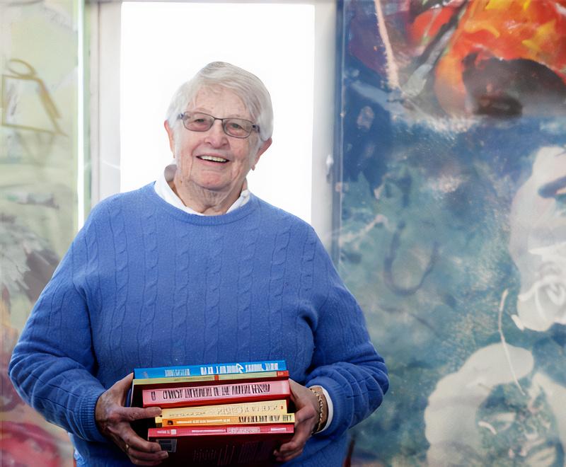 Portrait of Wiggsy Sivertsen wearing a blue sweater holding a stack of books.