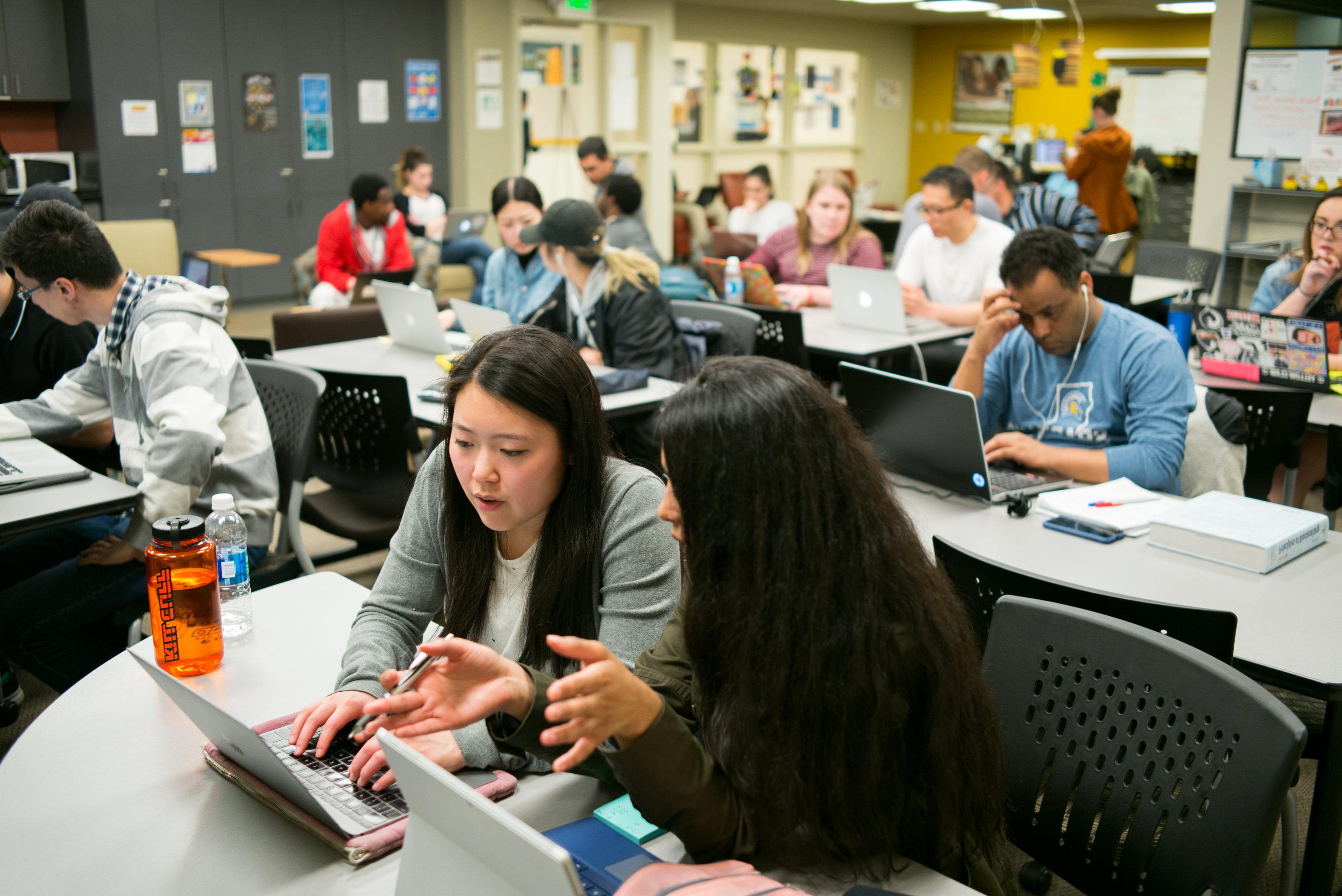 学生们坐在教室里一边看着笔记本电脑一边一起学习.